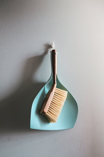 A person dressed in casual clothing and white socks is using a blue flat mop to clean a wooden floor inside a home, with a red cabinet visible in the background. The mop head appears to be damp, indic